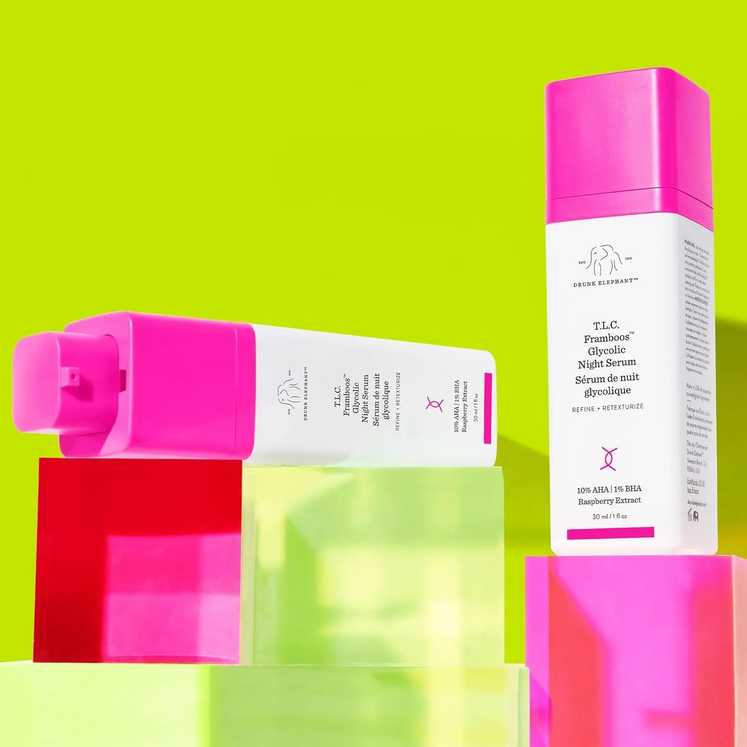 Drunk Elephant glycolic night serum bottles with pink caps displayed on colorful translucent blocks