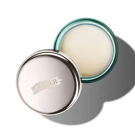 Open jar of La Mer lip balm with silver lid and soft balm inside on white background